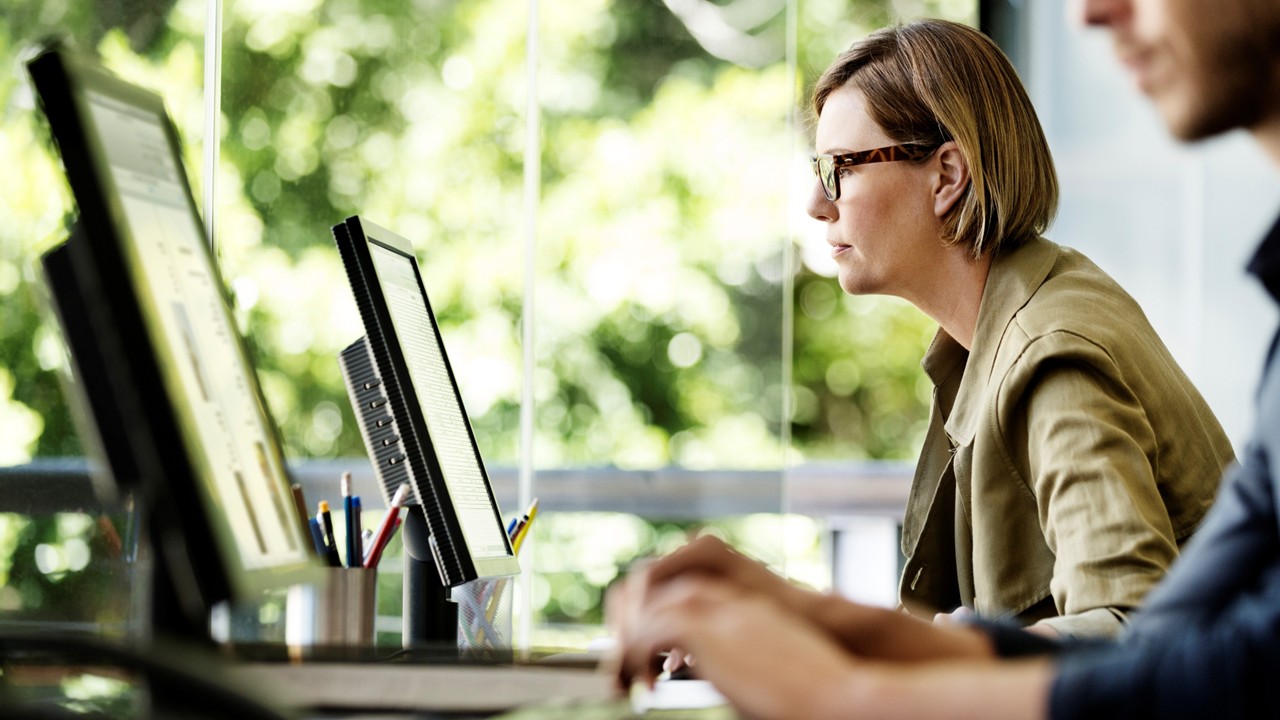 people working at computers with glass windows overlooking lush greenery